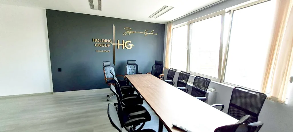 Заседателна зала на HOLDING GROUP с обемно златисто лого на тъмносиня стена